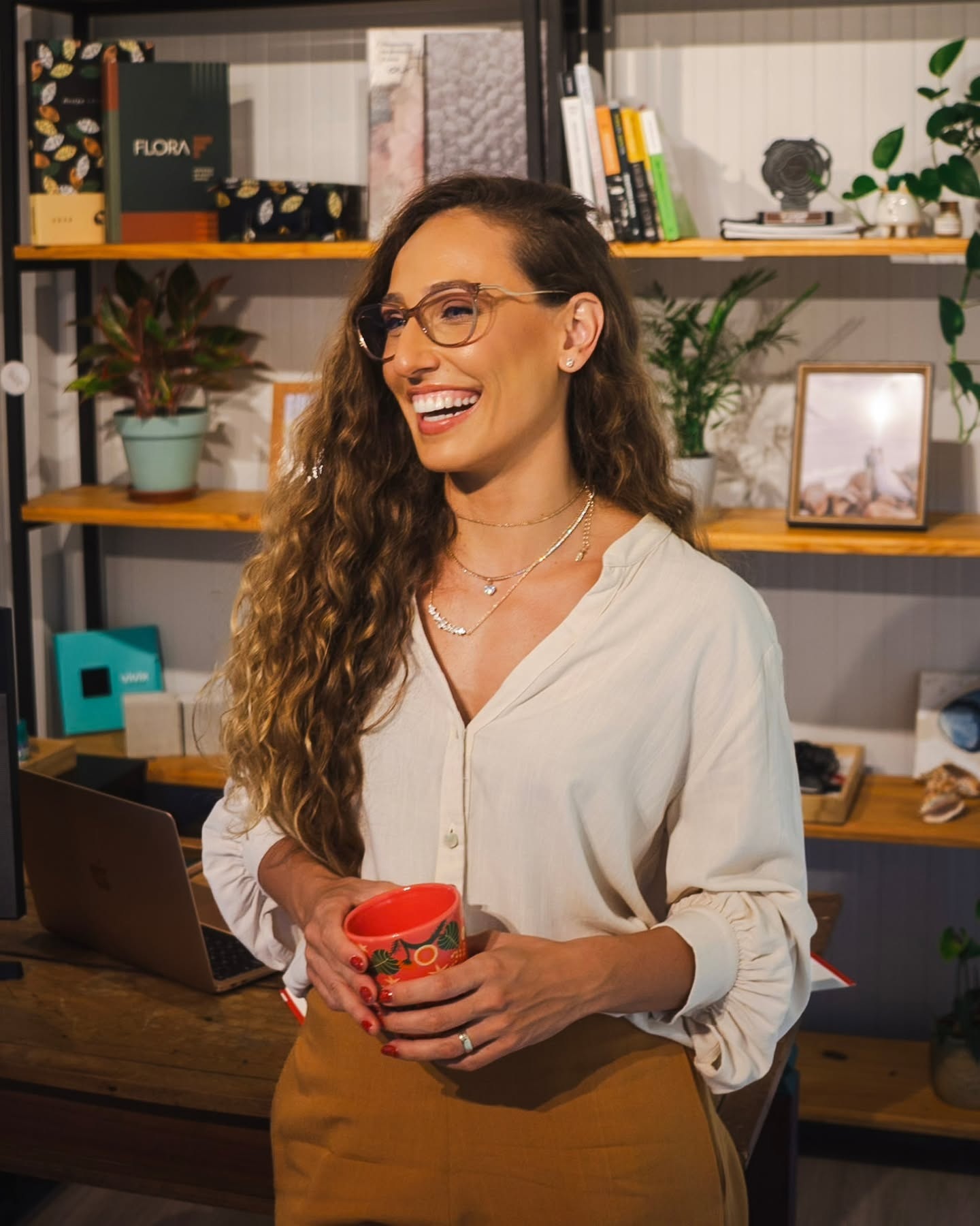 Andressa Tofarelli sorrindo em seu escritório, segurando uma caneca